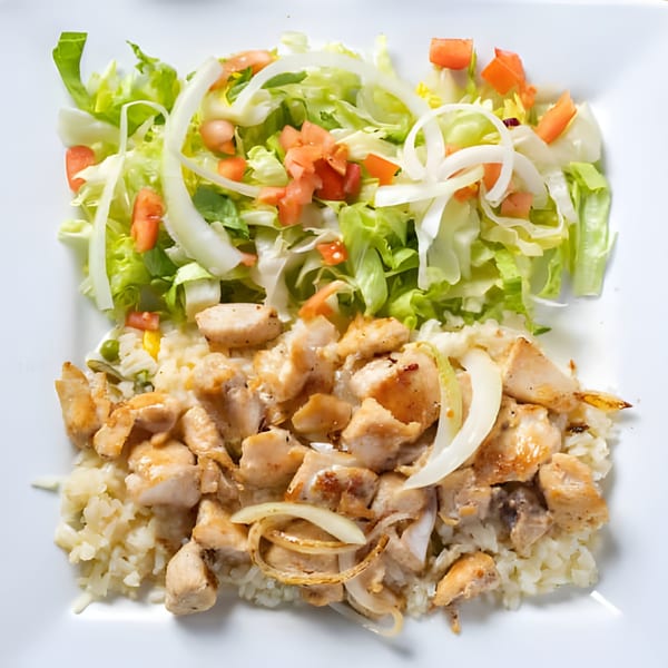 Chicken and rice with a side salad of lettuce, tomatoes, and onions on a white plate.