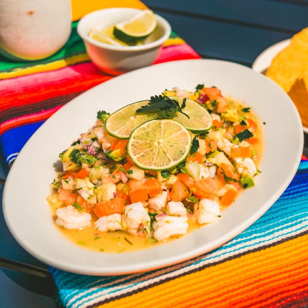 A vibrant plate of Tacos El Peladito ceviche with shrimp, tomatoes, and lime on a colorful Mexican serape.