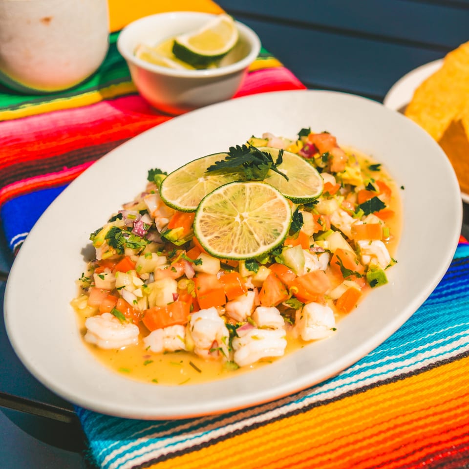 A vibrant plate of Tacos El Peladito ceviche with shrimp, tomatoes, and lime on a colorful Mexican serape.