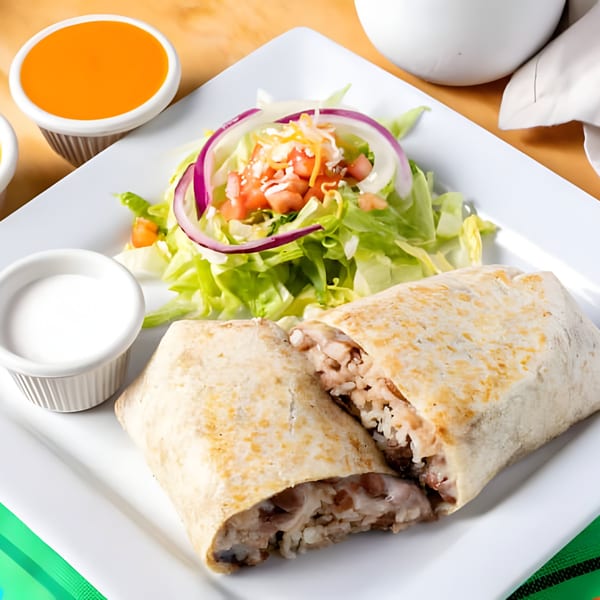 A large burrito, cut in half, revealing rice and meat, served with a side salad and sauces.